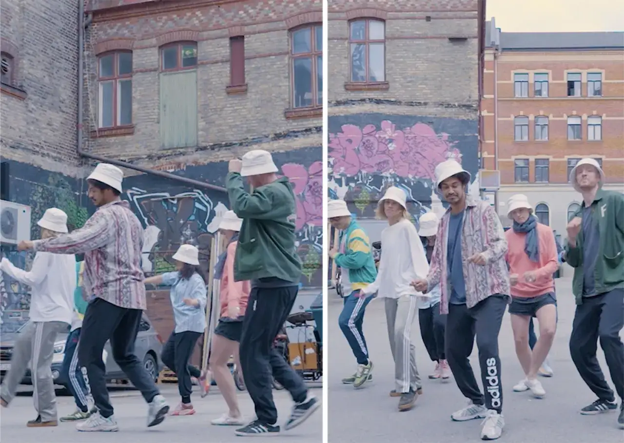 En grupp människor med hinkhattar dansar i en gränd i Stockholm. De rör sig synkroniserat till musiken, med en positiv och energisk atmosfär.