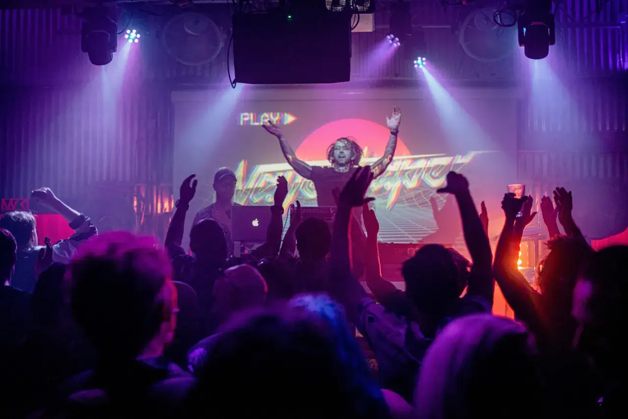 Publik jublar p&aring; en konsert i slaktkyrkan Stockholm. En DJ med armarna uppe framf&ouml;r en stor sk&auml;rm.