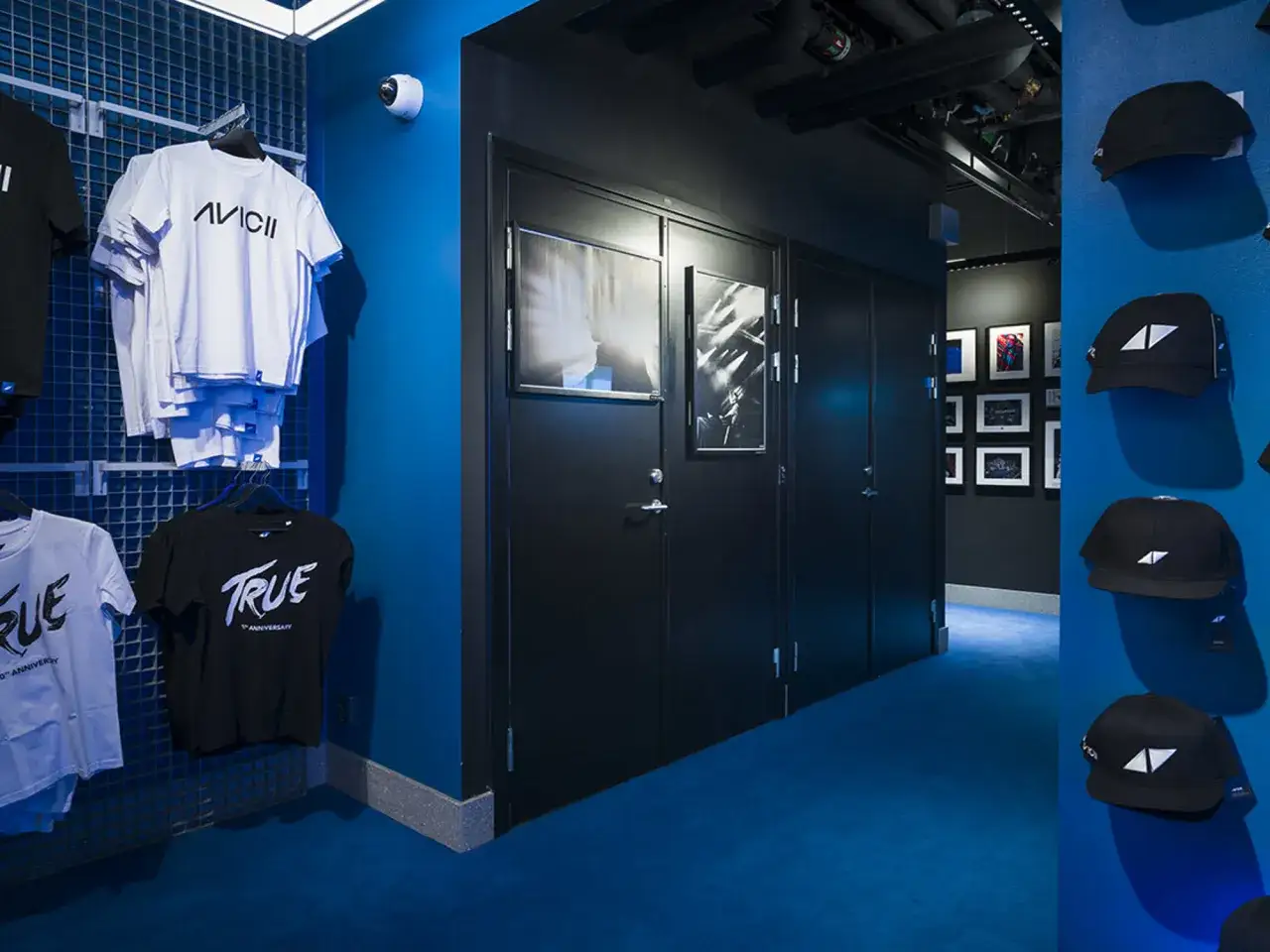 Avicii Experience-merchandise, som t-shirts och kepsar, hänger på väggar i ett blått rum.