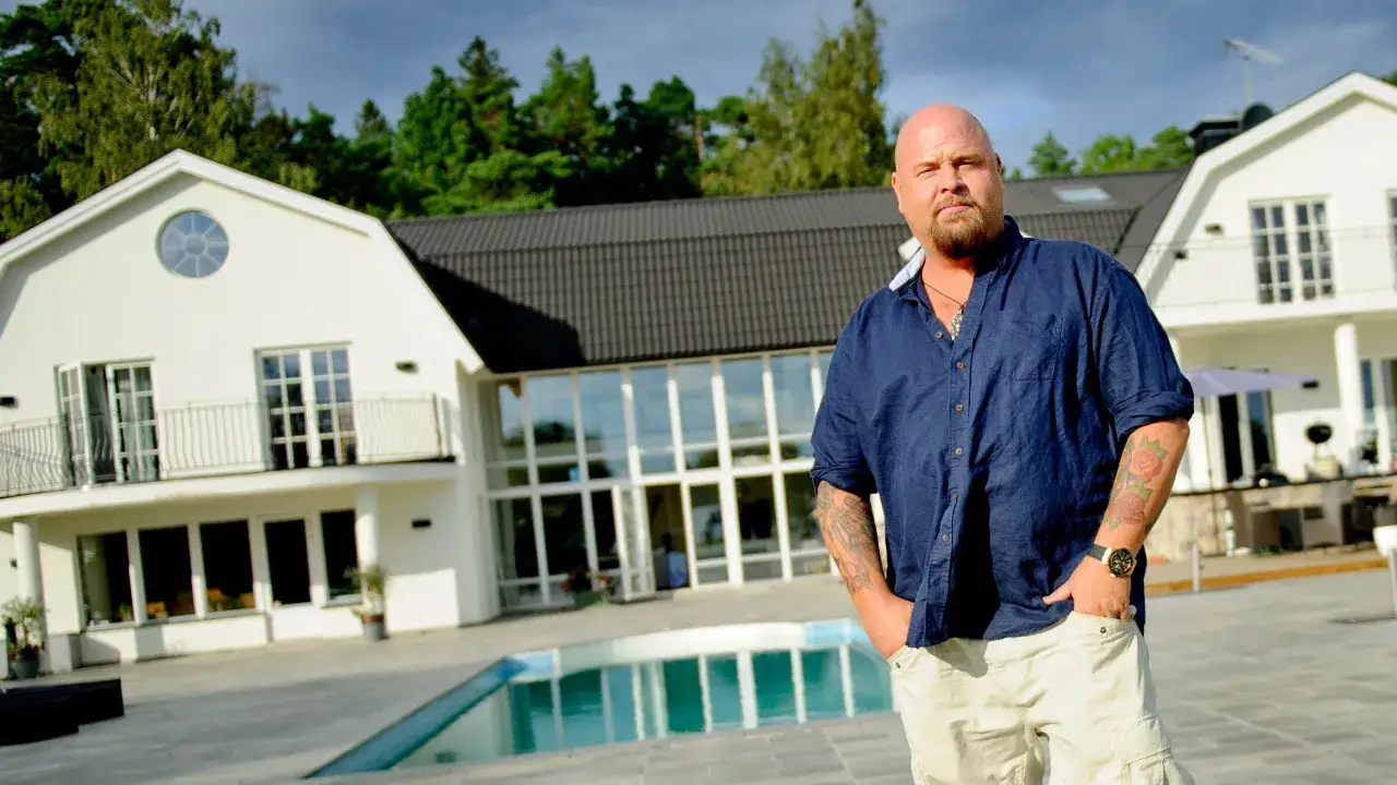 Man med tatueringar står framför ett modernt hus med pool. Kanske en framtida Rastaborgs slott?