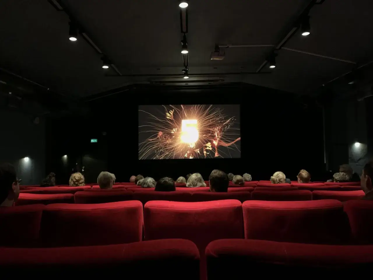 Publik njuter av en film på kulturhuset bio. En stor skärm visar en explosion av ljus och gnistor.