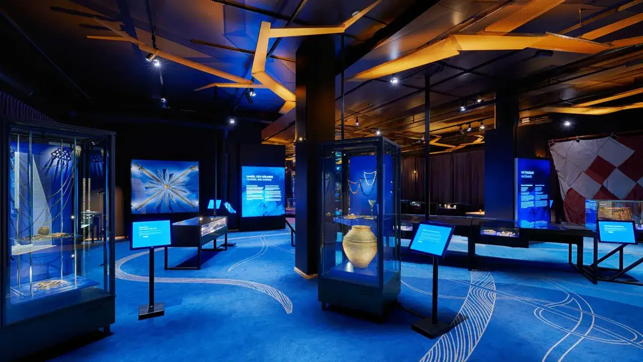 En utst&auml;llning om historiska museet vikingar med f&ouml;rem&aring;l i montrar och bl&aring; belysning.