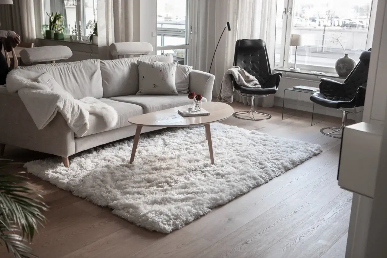 Mysigt vardagsrum med en ljusgrå soffa, fluffig matta och svarta läderfåtöljer.