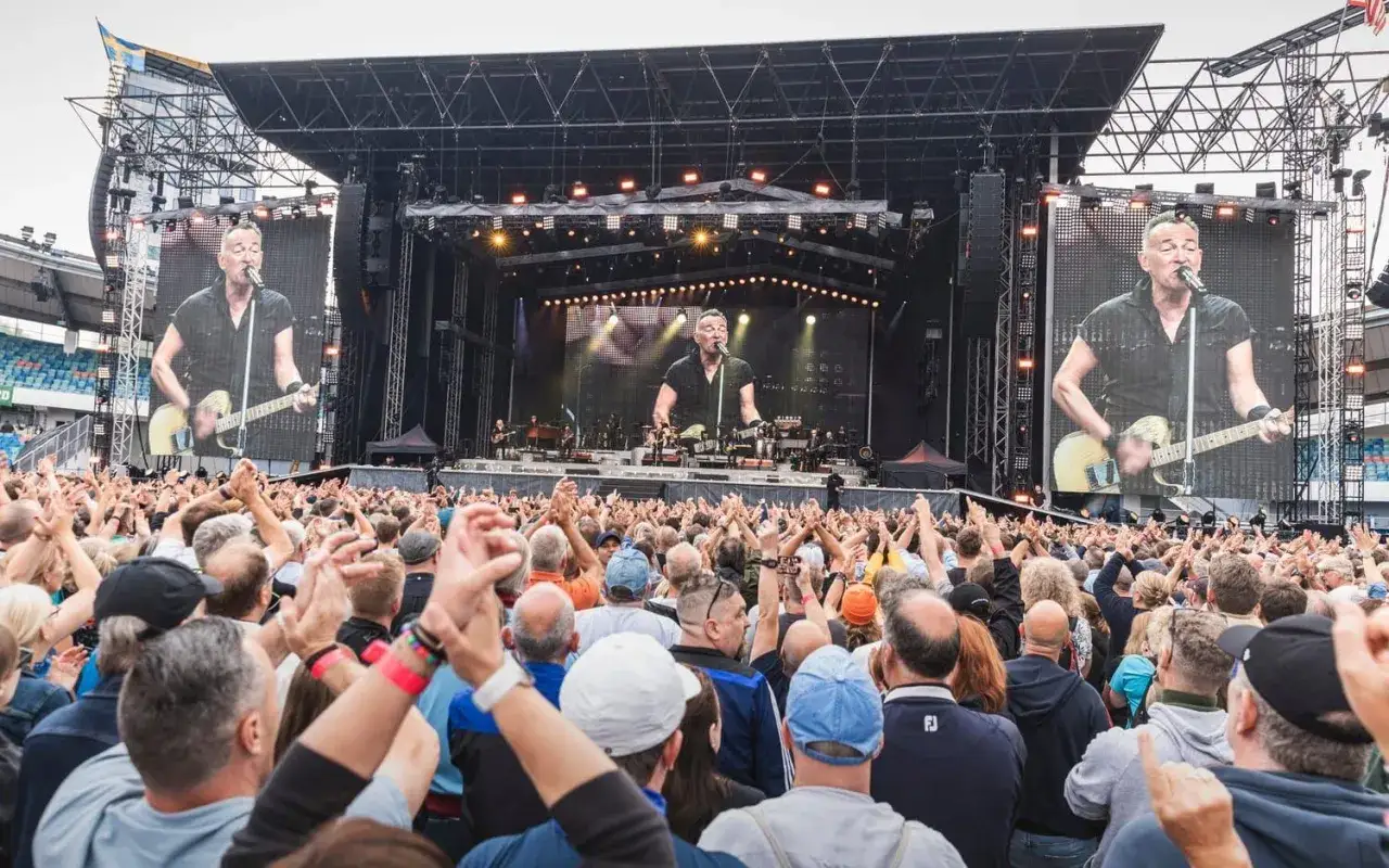 Publiken jublar under en Bruce Springsteen konsert. Stora sk&auml;rmar visar artisten som spelar gitarr.